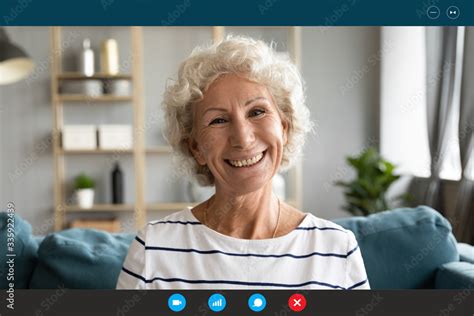Stockfoto Head Shot Old Granny Sit On Couch Smiles Looks At Webcam