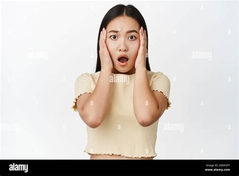 Shocked And Worried Asian Woman Gasping Looking Anxious At Camera Standing In Yellow T Shirt