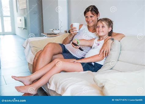 Mother And Her Daughter Are Watching Tv While Sitting On A Couch At Homehappy Mom And Her