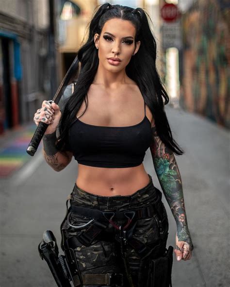 A Woman With Tattoos Holding A Baseball Bat And Wearing Black Pants On