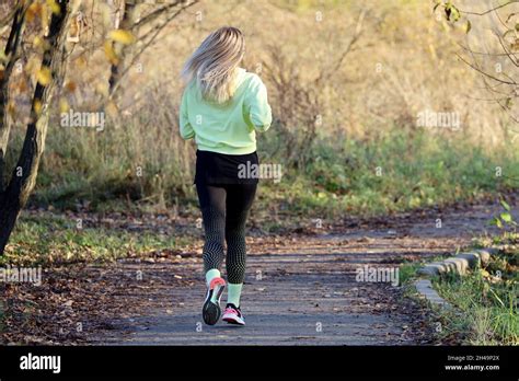 Blonde Girl Running In Autumn Park On Trees Background Rear View Alone Runner Concept Of