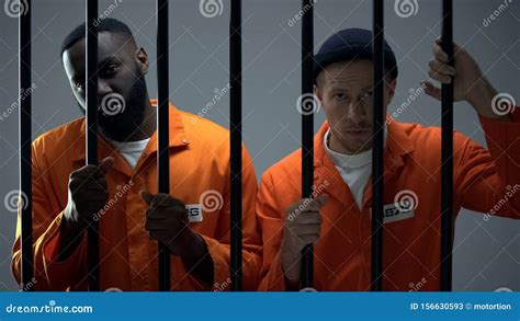 Caucasian And Afro American Prisoners Holding Jail Bars And Looking To