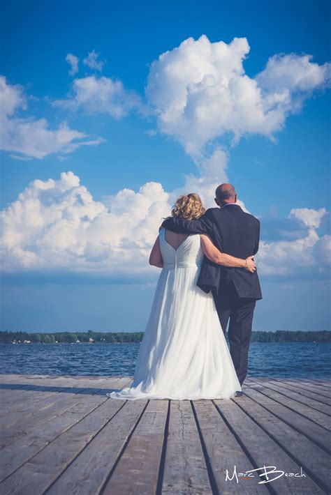 A Bride And Groom Standing On A Pier Looking Out At The Ocean Under A