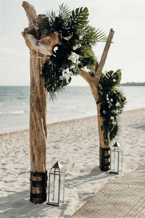 An Outdoor Ceremony Setup On The Beach With Lanterns And Greenery In