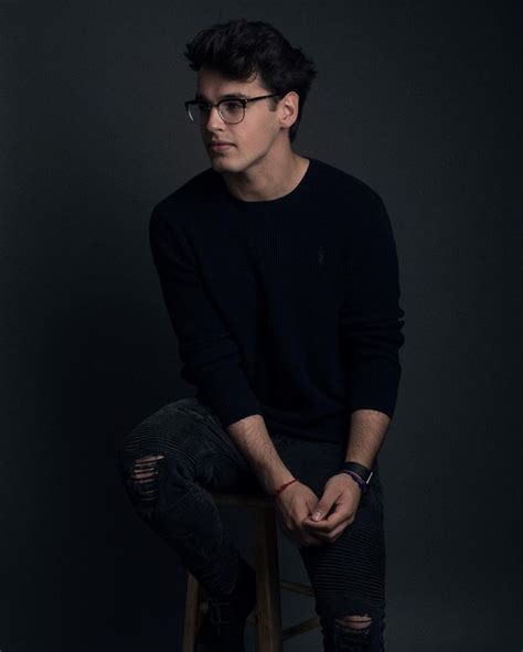 A Young Man Sitting On Top Of A Stool Wearing Black Jeans And A Black