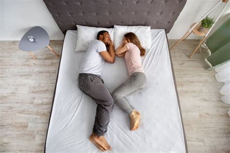 Full Length Of Affectionate Multiracial Couple Sleeping Together On Bed