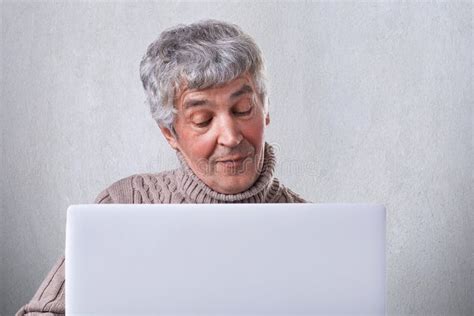 a satisfied old male having conversation online on his laptop while siting at home an