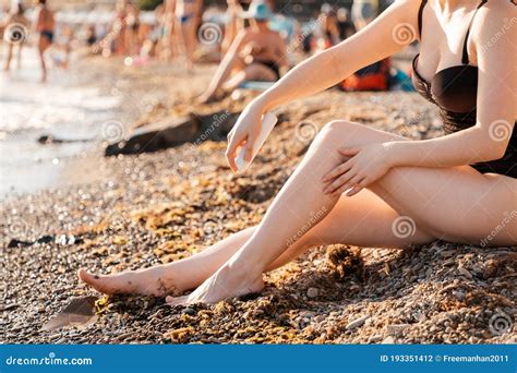 A Woman Sitting On The Beach By The Sea Uses A Cosmetic Product Legs