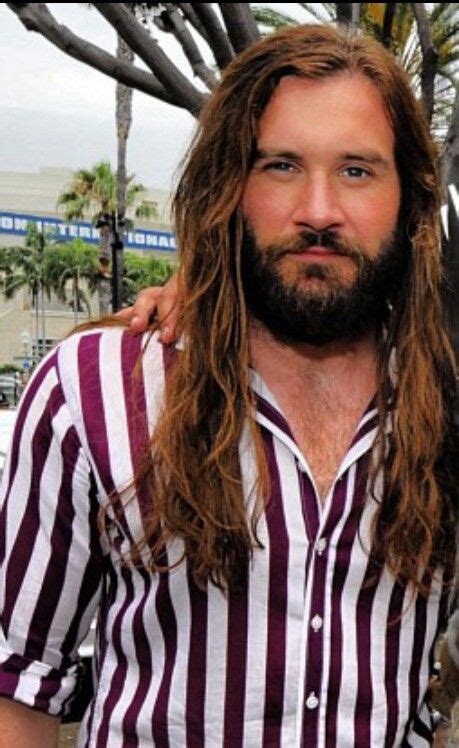 two men with long hair and beards standing next to each other in front of palm trees