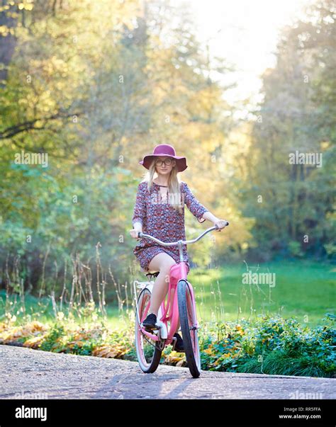 slim blond fashionable attractive woman in glasses short dress and pink hat riding lady bicycle
