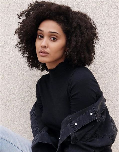 A Woman With Curly Hair Sitting On The Ground Wearing Jeans And A Black