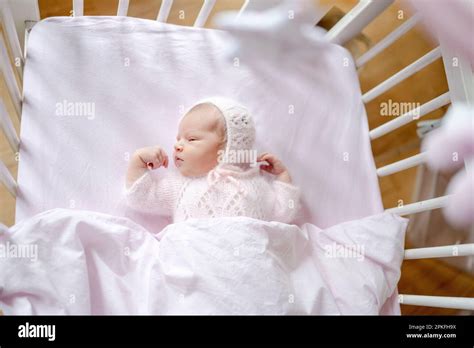 Newborn Baby Girl Wearing Knitted Hat Lying In Children Bed View From