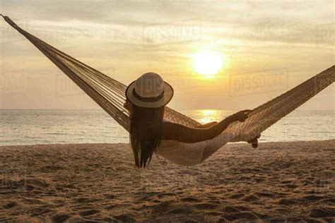 Rear View Of Woman Relaxing In Hammock At Beach During Sunset Stock