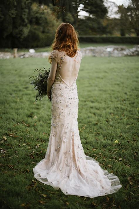 The Back Of A Woman In A Wedding Dress Holding A Bouquet And Standing On Grass