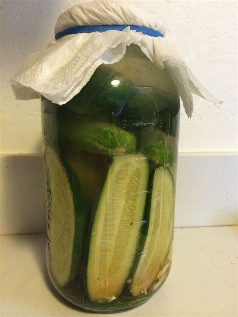 A Jar Filled With Cucumbers Sitting On Top Of A Counter Next To A White