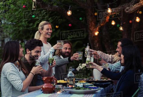 Multi Ethnic Friends Toasting Drinks At Dinner Table In Yard Stock