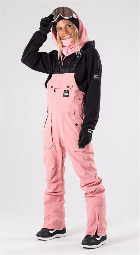 a woman in pink snow pants and ski goggles posing for the camera with her hands on her head