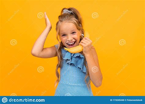 Vrolijk Meisje In Jurk Lookinf Noemt De Banaan Geïsoleerd Op Gele En Oranje Achtergrond Stock