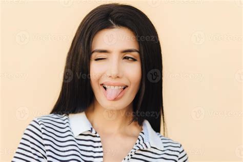 Funny Joyful Brunette Female Shows Tongue Blinks With Eye Makes Grimace Wears Braces Has