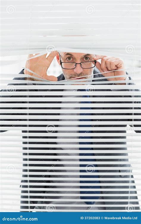 Portrait Of A Businessman Peeking Through Blinds In Office Stock Image