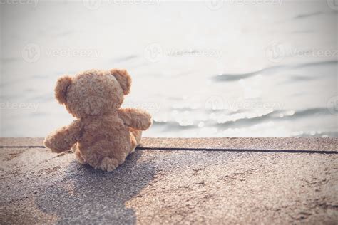 A Sad Teddy Bear Sits On A Bridge Alone Looking At The Sea In Lonely