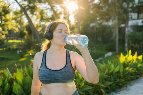 Overweight Woman Drinking Water After Jogging In The Park Portrait Of