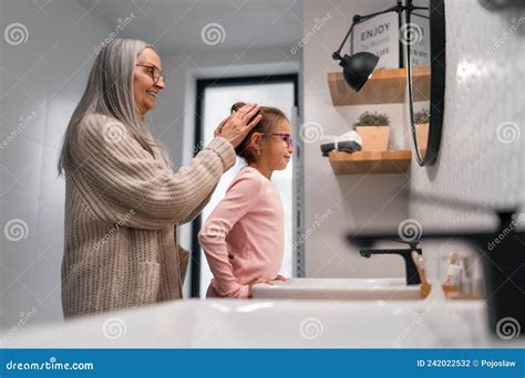 Senior Grandmother And Granddaughter Standing Indoors In Bathroom Daily Routine Concept Stock