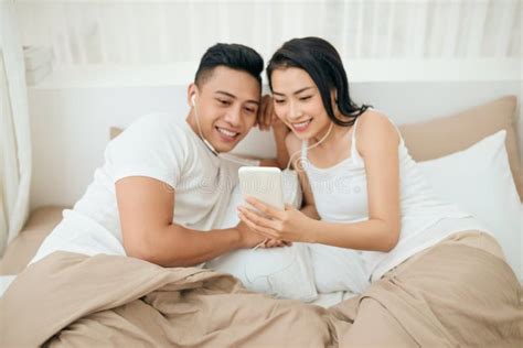 Indoor Photo Of Loving Couple Lying On White Sheets With Smartphone