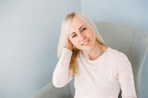 Beautiful Blonde Girl Sitting On Armchair In Light Blue Studio Stock