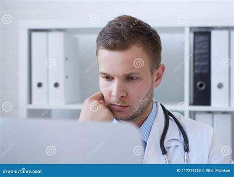 Young Serious Male Doctor Using Computer On Desk In Clinic Stock Image
