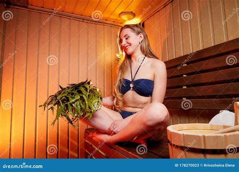 Beautiful Girl With Yellow Broom On Wooden Bench At Sauna In Steam Room