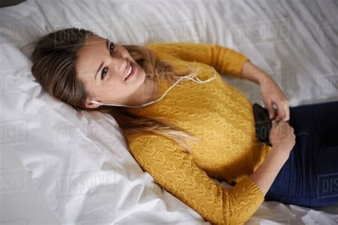 Portrait Of Teenage Girl Lying On Bed Listening To Earphones Stock