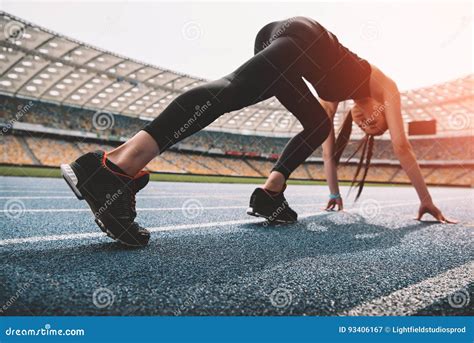 Young Woman In Sportswear In Starting Position On Running Track Stadium