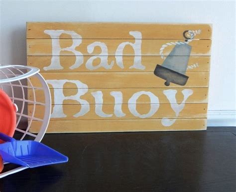 A Wooden Sign That Says Bad Buoy Next To An Orange And Blue Frisbee
