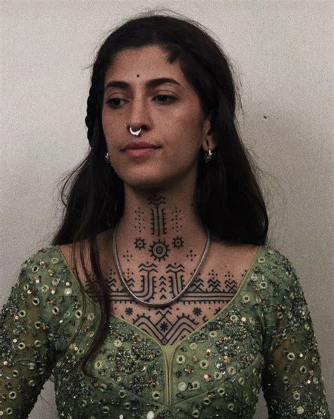 A Woman With Tattoos On Her Face And Chest Standing In Front Of A White Wall