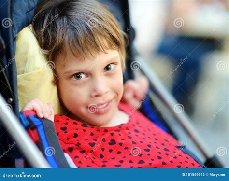A Disabled Child In A Wheelchair And A Cute Little Girl With Down