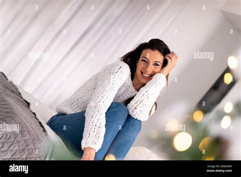 A Happy Beautiful Woman Sitting On The Bed During Christmas Season Beside A Christmas Tree Stock