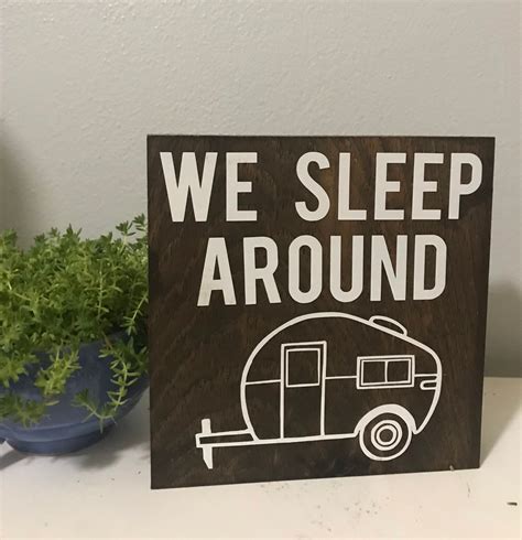 A Sign That Says We Sleep Around With A Camper In The Background Next