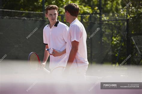Male Tennis Players With Tennis Rackets Talking On Sunny Tennis Court