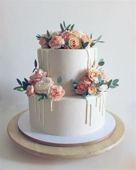 a three tiered white cake with flowers on top and dripping icing down the side
