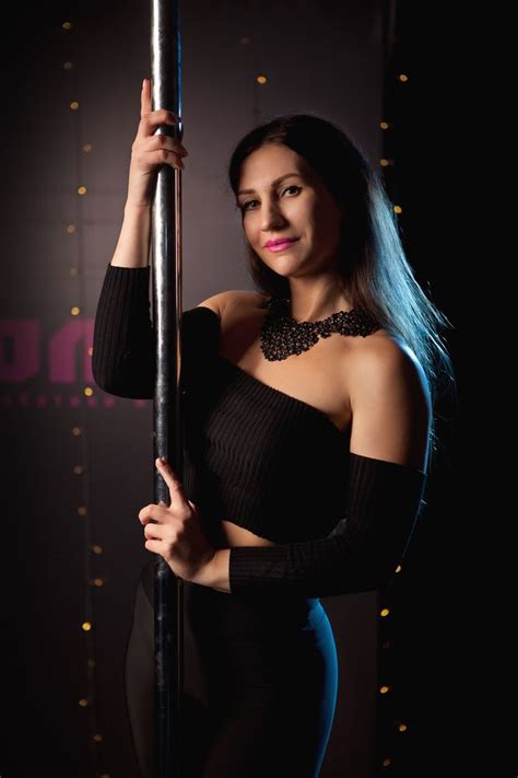 A Woman Posing With A Pole In Front Of A Dark Background At The End Of