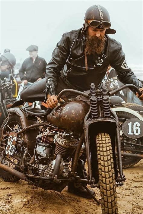 A Man Riding On The Back Of A Motorcycle Down A Dirt Road Next To Other Motorcycles