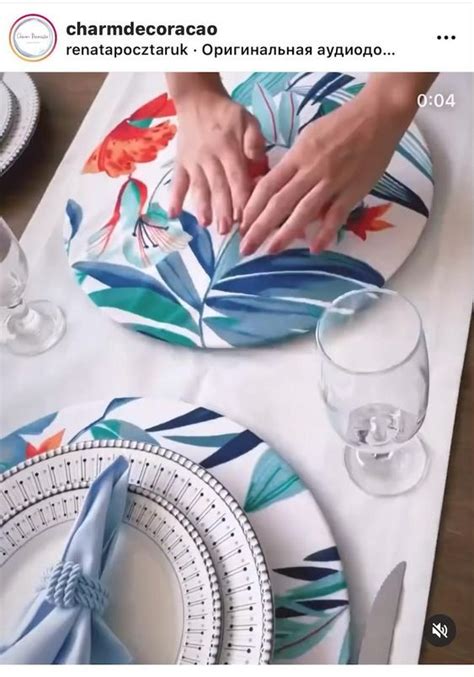 A Table With Plates And Napkins That Have Flowers On Them While Someone Places Their Hands On