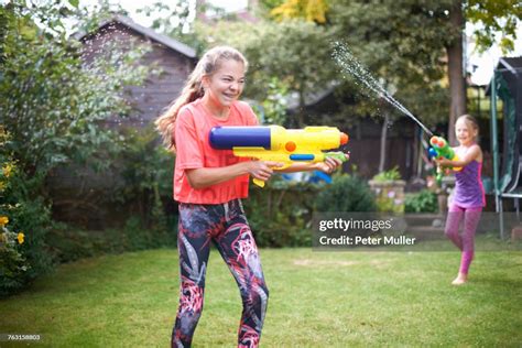 Teenage Girl And Her Sister Having Water Gun Fight In Garden High Res