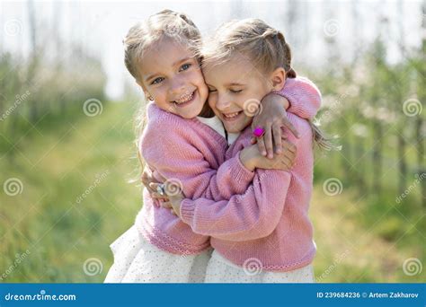 Happy Two Twin Sisters Are Hugging Against The Background Of A Green