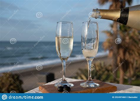 pouring of spanish cava sparkling wine is glasses with view on blue sea and sandy beach costa
