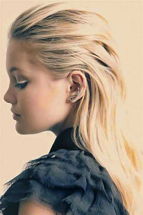 A Woman With Long Blonde Hair And Ear Piercings Looking Off To The Side