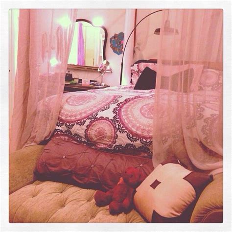 A Bed With Pink Curtains And A Teddy Bear Sitting On The Pillow In