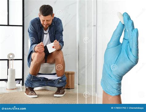 Doctor Holding Suppository For Hemorrhoid Treatment And Man Sitting On Toilet Bowl In Room Stock