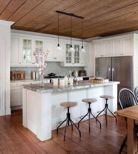 Wood and leather stools are placed at a beige veneer kitchen island finished with a black marble waterfall countertop positioned under a vaulted ceiling fitted with wood beams and skylights. New Home Interior Design: Cottage Kitchens